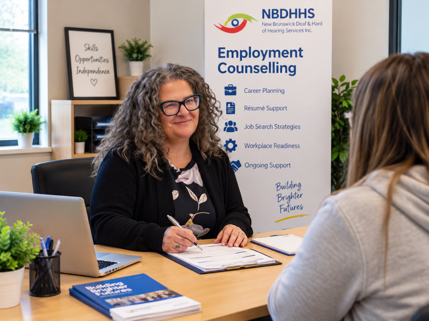 NBDHHS employment counsellor meeting with a client at a desk in front of an Employment Counselling banner